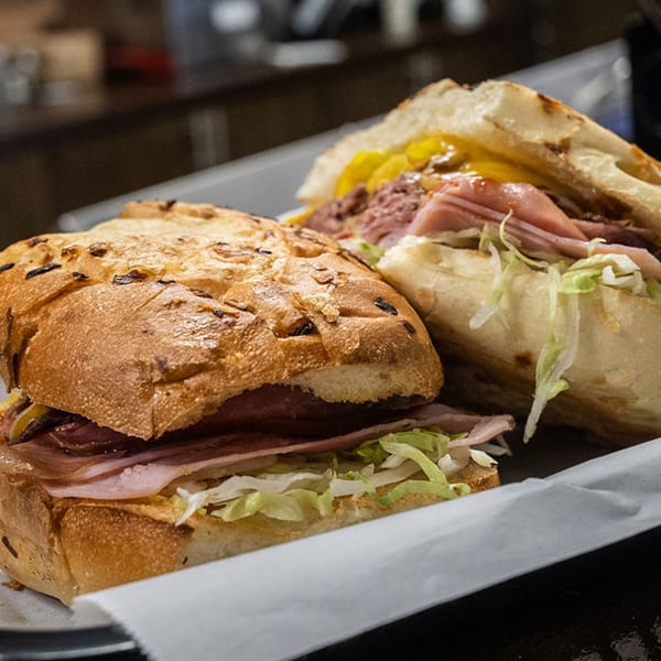 Two deli sandwiches on a tray, filled with meat, cheese, and shredded lettuce.