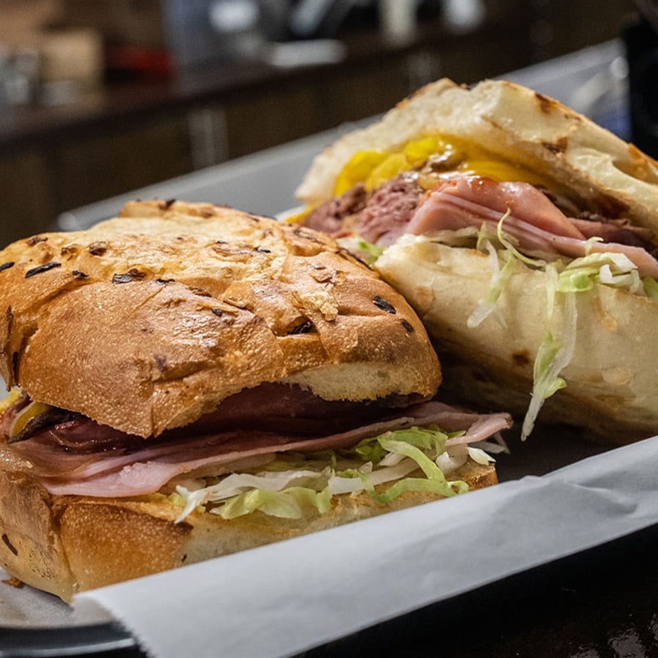 Two deli sandwiches on a tray, filled with meat, cheese, and shredded lettuce.